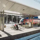 Winterliche Szene am **Lech Bahnhof**. Ein roter Zug steht bereit, während Reisende auf dem verschneiten Bahnsteig warten.