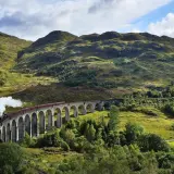 Dampfender Zug fährt über eine Bogenbrücke in den schottischen Highlands, auf dem Weg von Edinburgh in die malerische Landschaft.