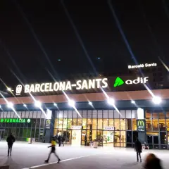 Nachts leuchtet die Barcelona-Sants Hauptbahnhof-Fassade mit den Logos von McDonald's und Farmacia.