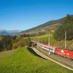 Roter ÖBB-Zug fährt durch eine grüne Alpenlandschaft. Die Strecke von Ljubljana nach Zagreb ist malerisch.