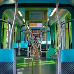 Innenraum eines modernen Zuges in Luxemburg mit blauen und grünen Sitzen, polierten Metallstangen und Bildschirmen.