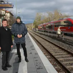 Zwei Männer stehen auf dem Bahnsteig des kleinsten Bahnhofs Deutschlands. Ein roter Zug der Westfrankenbahn wartet auf Fahrgäste.