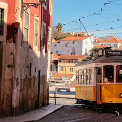 Gelber Straßenbahnwagen Nr. 28 fährt durch die engen Gassen Lissabons, vorbei an historischen Gebäuden und mit Blick auf die Basilika Estrela.