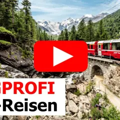 Roter Zug fährt über eine Steinbrücke durch eine Berglandschaft mit Wasserfall. Einer der besten landschaftlichen Zugfahrten.