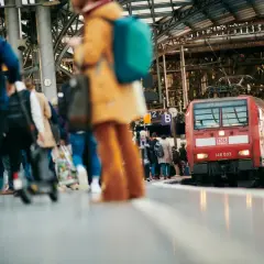Menschen warten auf dem Bahnsteig auf ihre **Reise im Zug**. Eine rote Lokomotive der Deutschen Bahn steht bereit.
