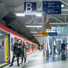 Rote S-Bahn am Bahnsteig, bereit für die Fahrt zum Flughafen München. Schilder weisen den Weg.
