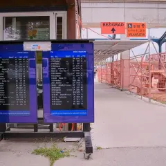 Anzeigetafeln am Bahnhof Ljubljana zeigen Abfahrts- und Ankunftszeiten. Baustellenabsperrungen und ein Bagger sind im Hintergrund sichtbar.