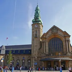 Der imposante **luxembourg train station** mit seinem Uhrturm und der großen Fensterfront, belebt von Reisenden unter blauem Himmel.