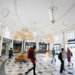 Menschen eilen durch den hellen, modernen **Coburger Bahnhof** mit seinen auffälligen Lampen und Sitzgelegenheiten.