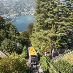 Gelbe Standseilbahn fährt bergauf, Blick auf Comer See und Bahnhof.