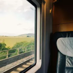 Blick aus dem Fenster eines Zuges auf dem Weg nach Hamburg. Grüne Felder und ein bewölkter Himmel ziehen vorbei.
