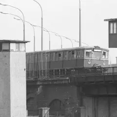 Eine Bahn fährt über eine Brücke, vorbei an Grenztürmen. Ein Symbol für die Zeit vor dem Mauerfall.