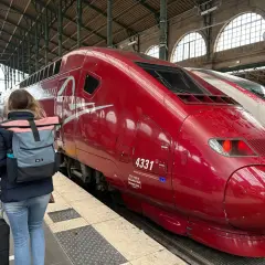Roter Thalys-Zug am Bahnsteig, bereit für die Fahrt von Stuttgart nach Strasbourg. Eine Reisende mit Rucksack und Gepäck wartet.