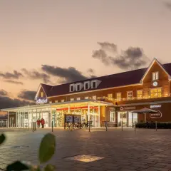 Der Bahnhof Nordhorn im Abendlicht, mit beleuchteten Fenstern und einem Schild "Bahnhof".