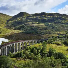 Dampfender Zug fährt über eine Bogenbrücke in den schottischen Highlands, auf dem Weg von Edinburgh in die malerische Landschaft.