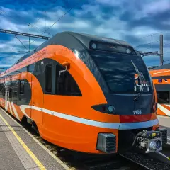 Moderner, orange-grauer latvia train steht am Bahnsteig unter blauem Himmel mit Wolken.