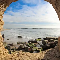 Blick aus einer Höhle am Strand von Rom. Wellen brechen an Felsen.