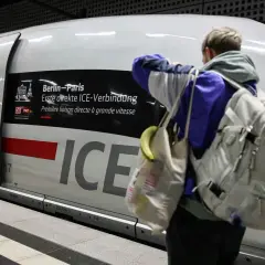 Ein Reisender mit Rucksack und Tasche steht vor dem ICE, der als "Berlin-Paris Erste direkte ICE-Verbindung" beworben wird.