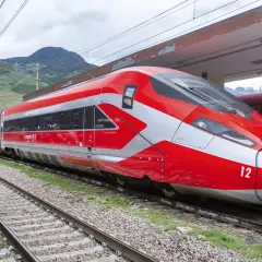 Roter Hochgeschwindigkeitszug mit silbernen Akzenten steht am Bahnsteig. Perfekt für eine entspannte Zug Rundreise durch die Berge.