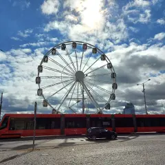 Rotes Tram fährt am Bratislava Hauptbahnhof vorbei, ein Riesenrad im Hintergrund.