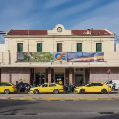 Gelbe Taxis warten vor dem Bahnhof Athen. Ein Schild verkündet "Wir transformieren unser Schienennetz, wir modernisieren Transporte".