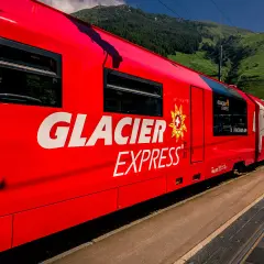 Der rote Glacier Express fährt durch eine grüne Berglandschaft.