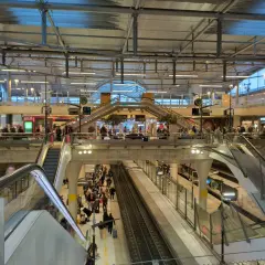 Menschenmassen auf einem Bahnhof, bereit für die Reise mit dem Zug nach Disneyland Paris. Rolltreppen und Bahnsteige sind voller Reisender.