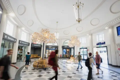 Menschen eilen durch den hellen, modernen **Coburger Bahnhof** mit seinen auffälligen Lampen und Sitzgelegenheiten.