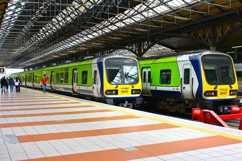Zwei grüne und blaue Züge stehen auf einem Bahnsteig unter einem großen Dach.