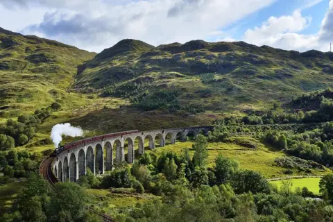 Dampfender Zug fährt über eine Bogenbrücke in den schottischen Highlands, auf dem Weg von Edinburgh in die malerische Landschaft.