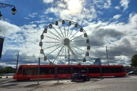 Rotes Tram fährt am Bratislava Hauptbahnhof vorbei, ein Riesenrad im Hintergrund.