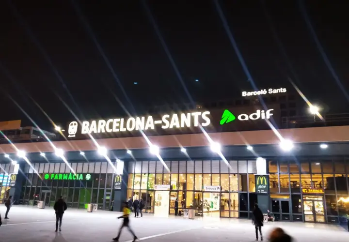 Nachts leuchtet die Barcelona-Sants Hauptbahnhof-Fassade mit den Logos von McDonald's und Farmacia.