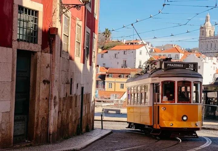 Gelber Straßenbahnwagen Nr. 28 fährt durch die engen Gassen Lissabons, vorbei an historischen Gebäuden und mit Blick auf die Basilika Estrela.