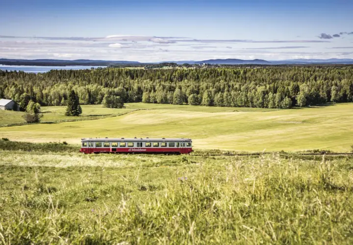 Ein roter Zug fährt durch eine grüne Landschaft in Schweden. Die #Inlandsbanan ist eine malerische Strecke.