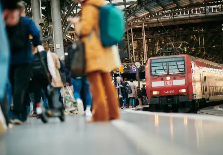 Menschen warten auf dem Bahnsteig auf ihre **Reise im Zug**. Eine rote Lokomotive der Deutschen Bahn steht bereit.