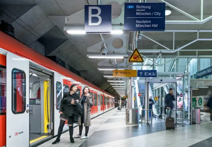 Rote S-Bahn am Bahnsteig, bereit für die Fahrt zum Flughafen München. Schilder weisen den Weg.