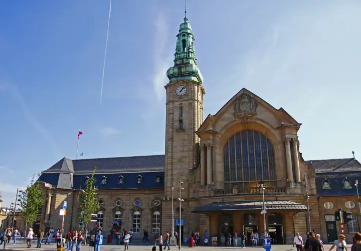 Der imposante **luxembourg train station** mit seinem Uhrturm und der großen Fensterfront, belebt von Reisenden unter blauem Himmel.
