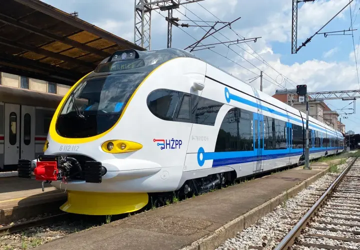 Moderner weiß-blauer kroatischer Zug (HŽPP) steht am Bahnsteig.