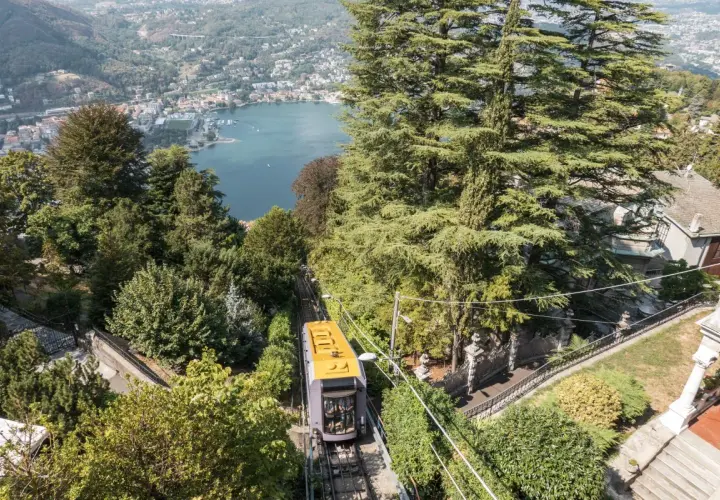 Gelbe Standseilbahn fährt bergauf, Blick auf Comer See und Bahnhof.