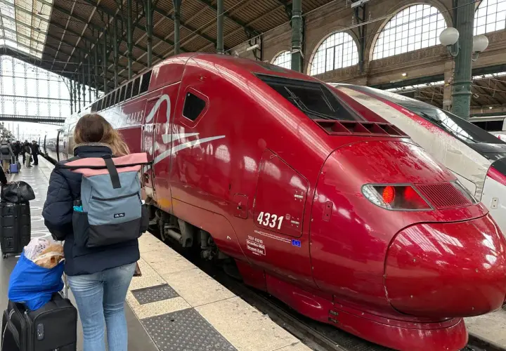 Roter Thalys-Zug am Bahnsteig, bereit für die Fahrt von Stuttgart nach Strasbourg. Eine Reisende mit Rucksack und Gepäck wartet.