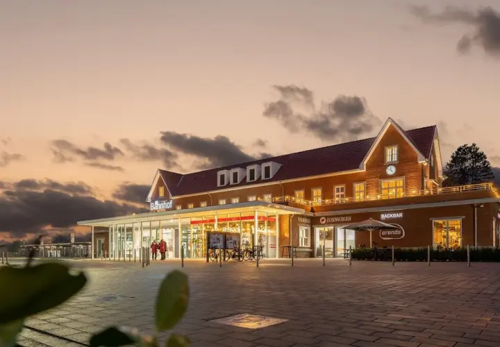 Der Bahnhof Nordhorn im Abendlicht, mit beleuchteten Fenstern und einem Schild "Bahnhof".