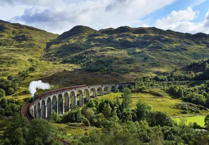 Dampfender Zug fährt über eine Bogenbrücke in den schottischen Highlands, auf dem Weg von Edinburgh in die malerische Landschaft.