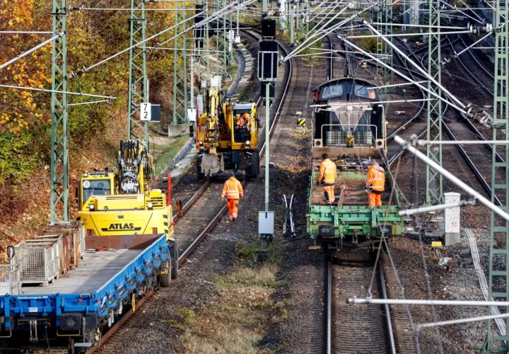 Arbeiter in orangefarbenen Warnwesten inspizieren Gleise neben Baumaschinen und Zügen. Die Szene zeigt die Infrastruktur der serbischen Eisenbahnen im Herbst.