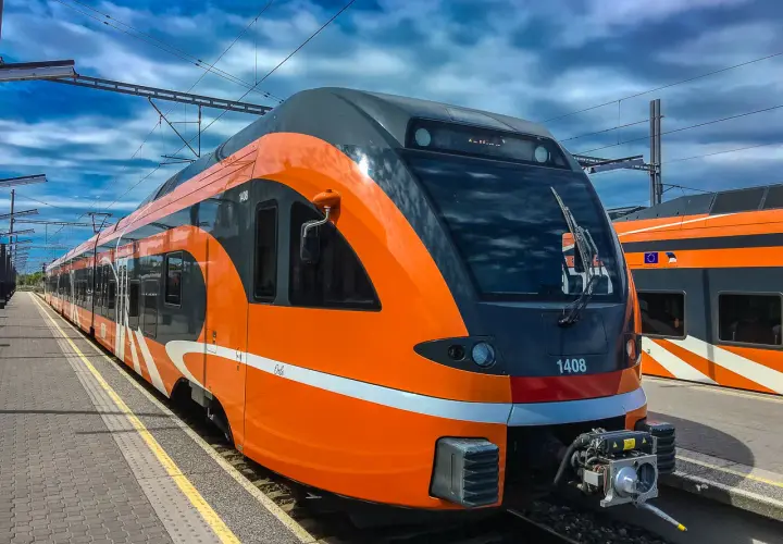 Moderner, orange-grauer latvia train steht am Bahnsteig unter blauem Himmel mit Wolken.