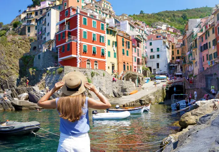 Frau mit Strohhut blickt auf bunte Häuser am Meer in Italien. Die Reise mit dem Zug ans Meer war die perfekte Idee für diesen Urlaub.