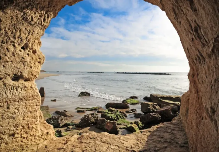 Blick aus einer Höhle am Strand von Rom. Wellen brechen an Felsen.