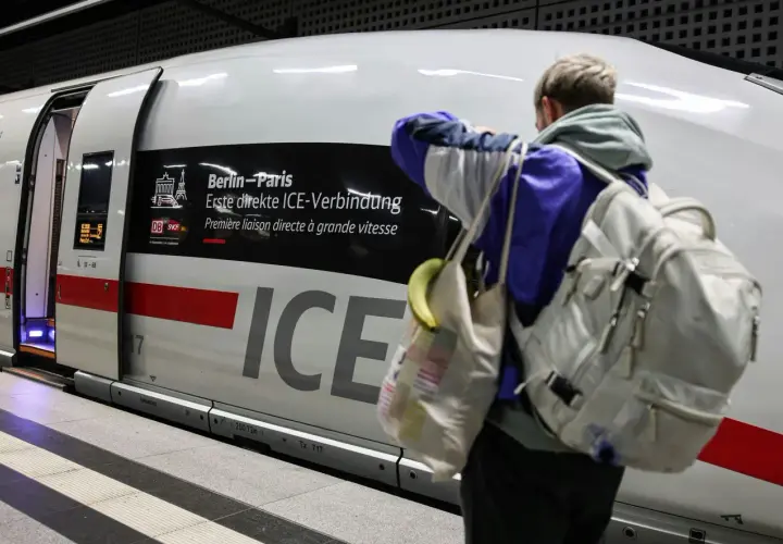 Ein Reisender mit Rucksack und Tasche steht vor dem ICE, der als "Berlin-Paris Erste direkte ICE-Verbindung" beworben wird.