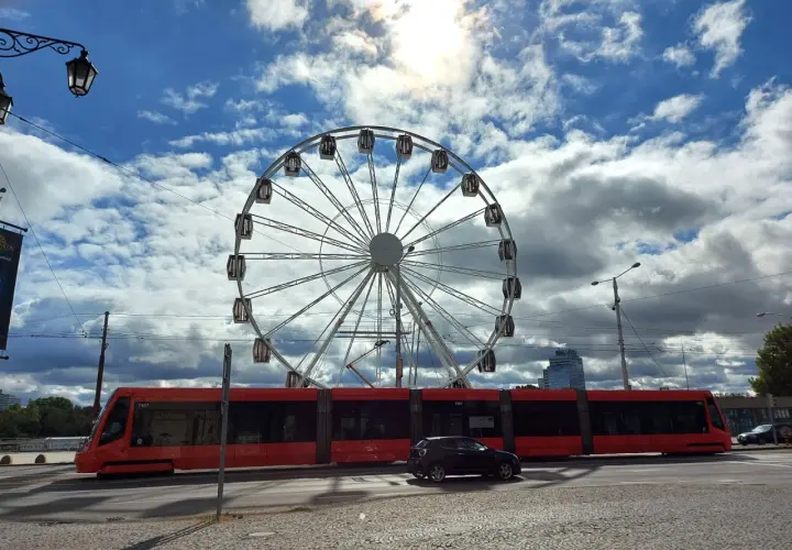 Rotes Tram fährt am Bratislava Hauptbahnhof vorbei, ein Riesenrad im Hintergrund.