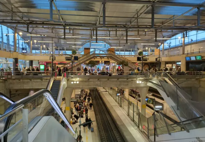 Menschenmassen auf einem Bahnhof, bereit für die Reise mit dem Zug nach Disneyland Paris. Rolltreppen und Bahnsteige sind voller Reisender.