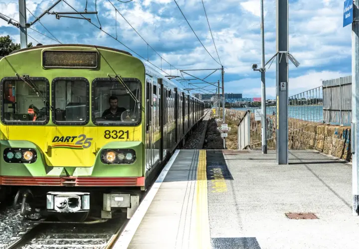 Grüner irischer Zug DART 25 mit der Nummer 8321 fährt auf einer Strecke am Meer entlang.